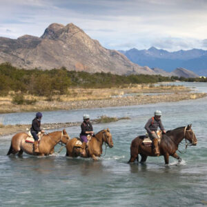 Tres personas cruzando el Río Meliquina sobre caballos.